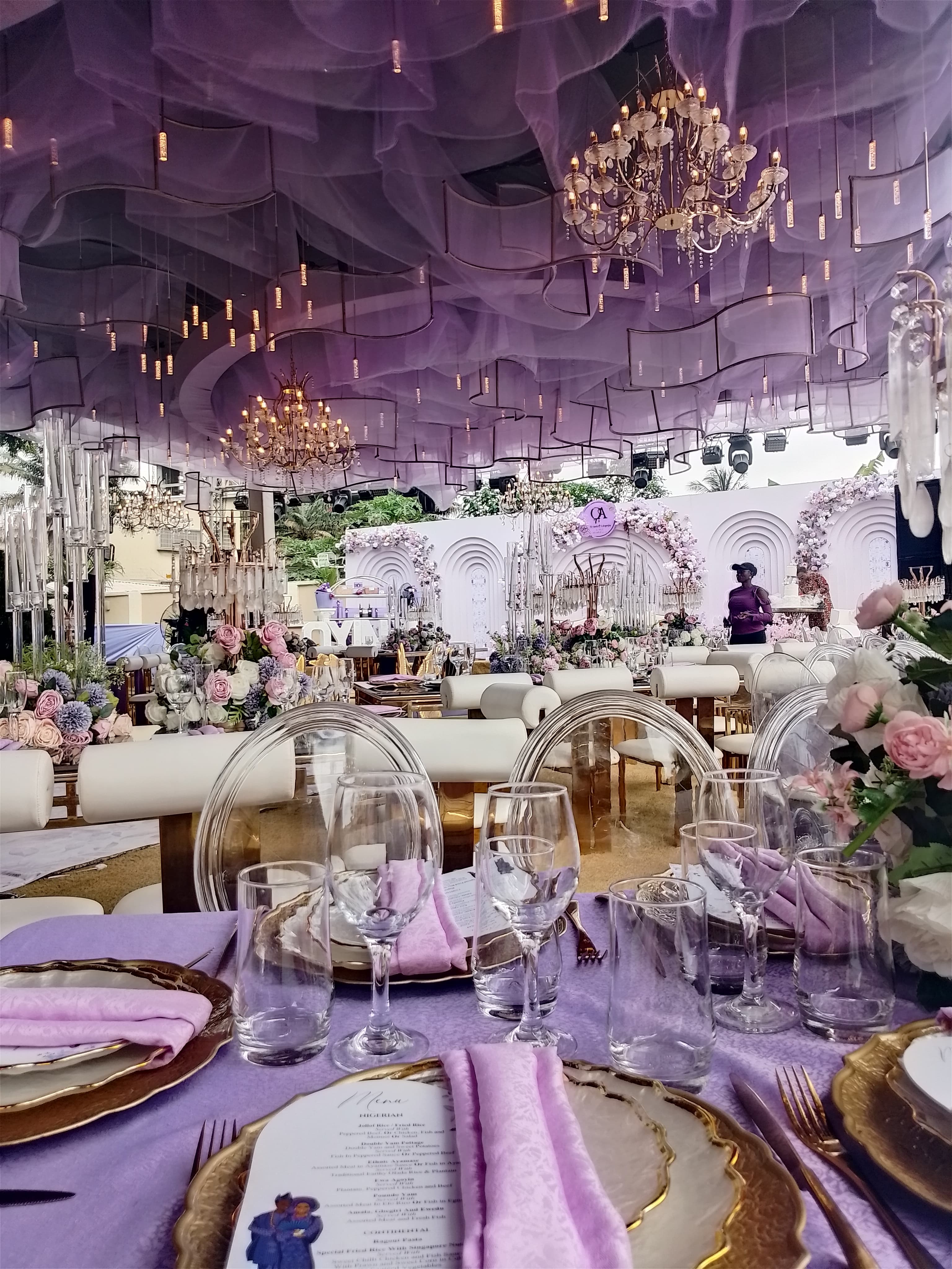 Lavish event hall with purple fabric ceiling drapes, crystal chandeliers, and formal gold-rimmed table settings.