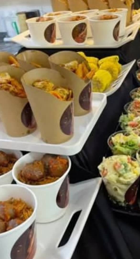 Assorted catering appetizers including fried food cones, meatball cups, and small salads on white trays.