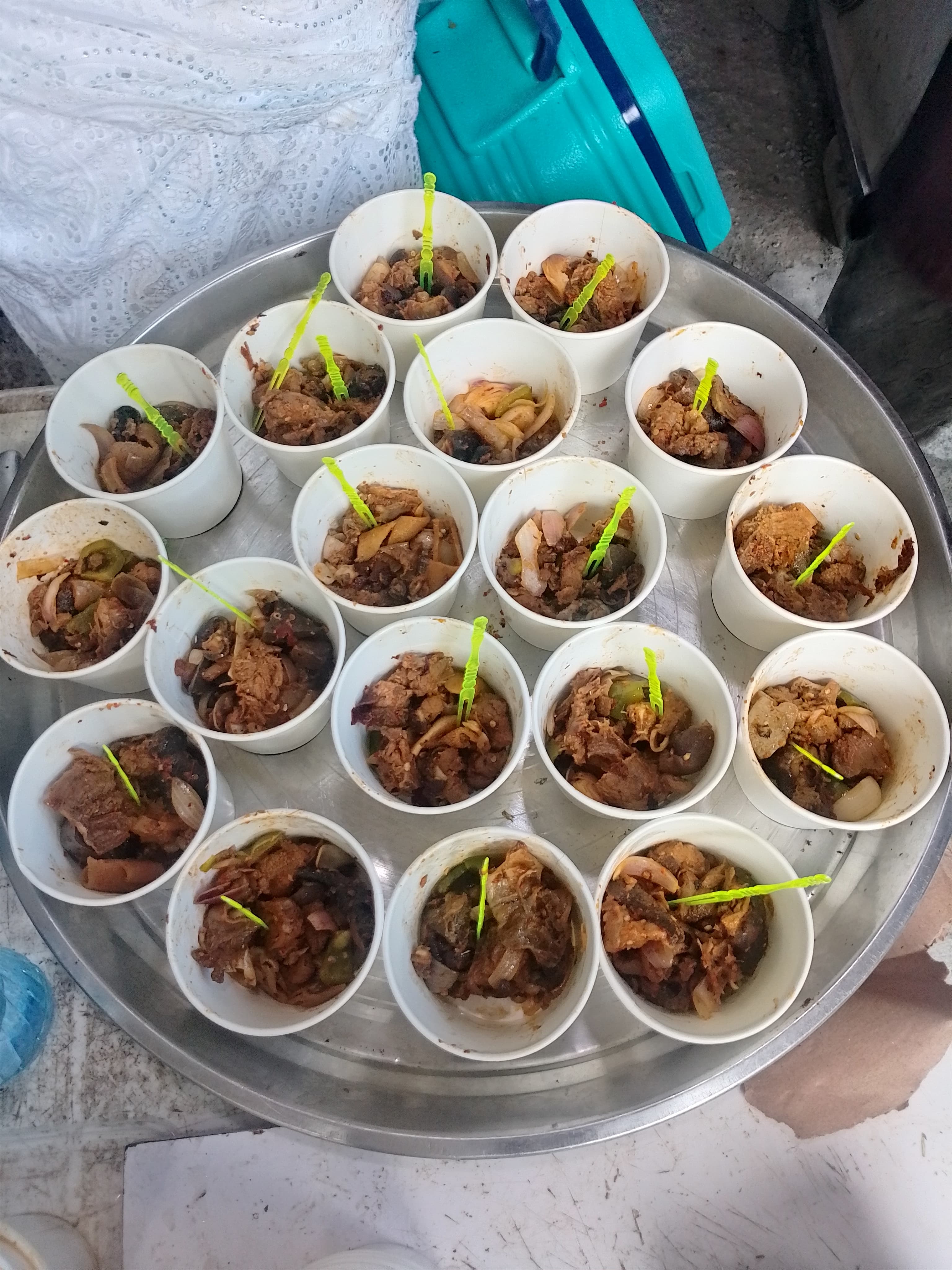 Silver tray holding small white cups of cooked meat and vegetables with green plastic forks.